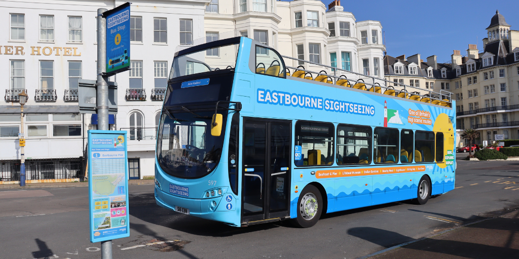 Eastbourne Sightseeing bus with blue and beach themed wrapped parked at bus stop with blue pole in front of white hotel