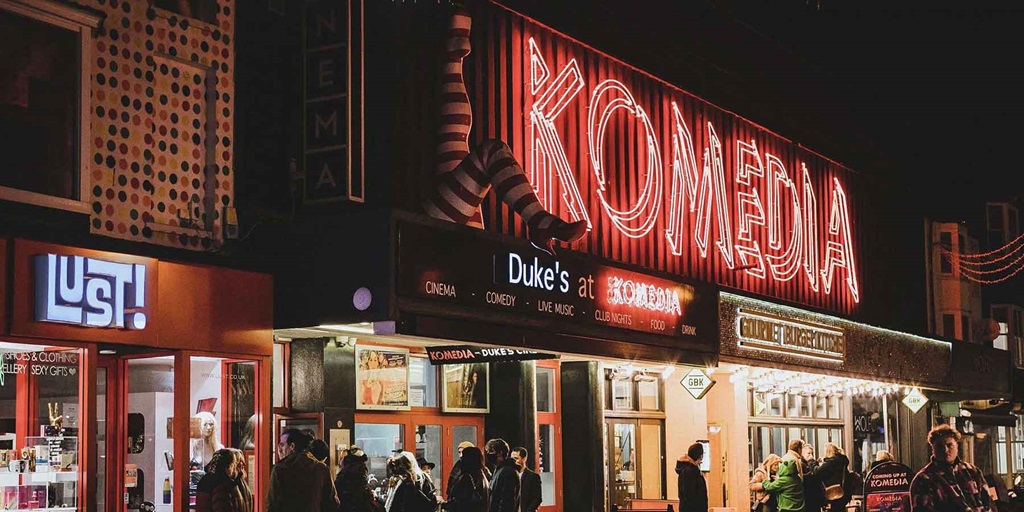 Komedia lit up in red with people walking past in the street.