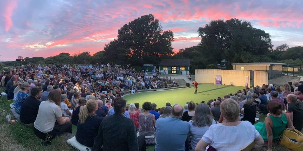 Overview of the theatre with the sun setting in the background and people sitting watching the performance.