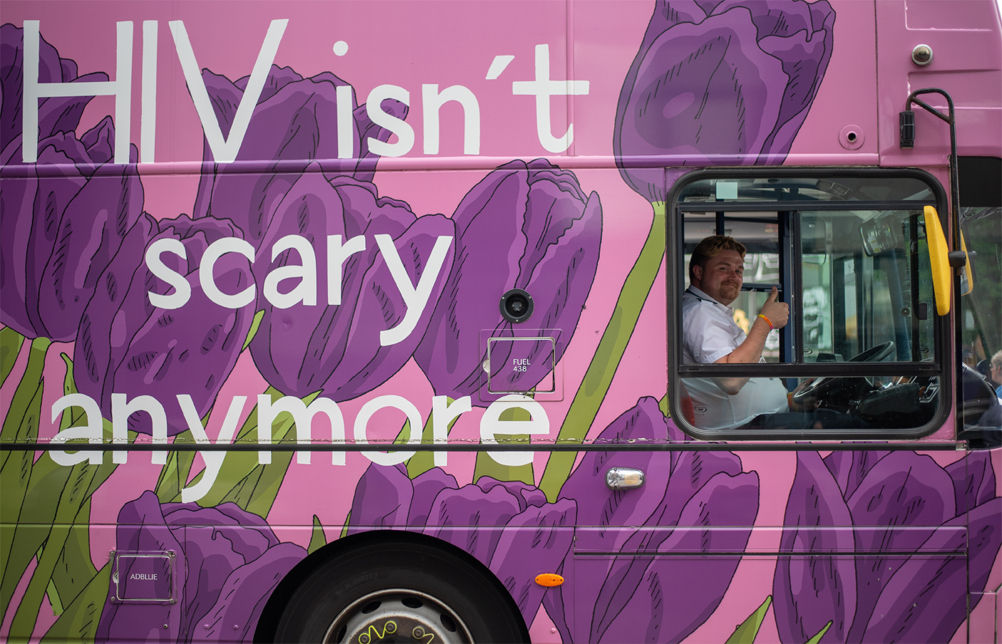 Bus with writing that says 'HIV isn't scary anymore' with a driver inside giving a thumbs up to the camera